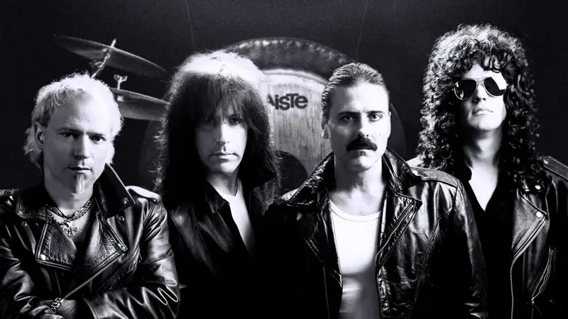 Black-and-white photo of the four members of Almost Queen in leather jackets in front of a drum kit and gong