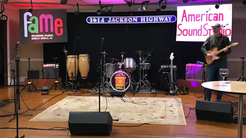 A band setup with drums, congas, amps and microphones on a wood floor in the hall, with Muscle Shoals-themed banners behind