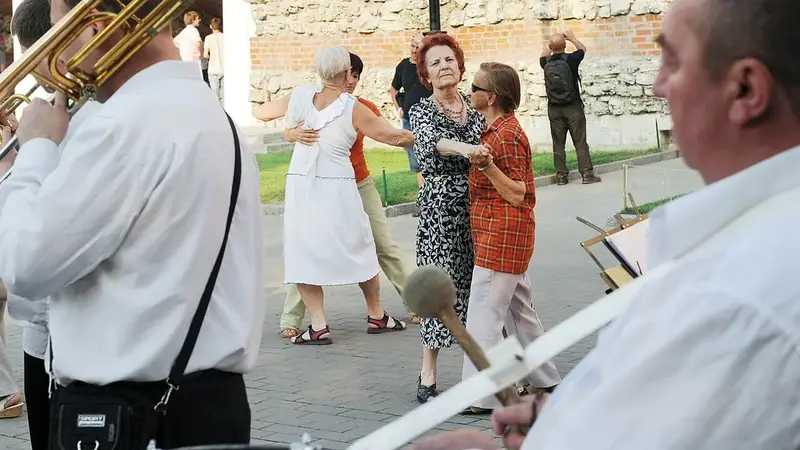 Older couples waltz on a stone plaza in a park while a brass band plays in the foreground