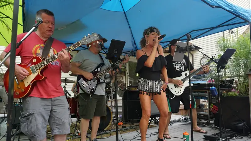 Beer Nutz playing outdoors under a blue tent, the singer at the microphone between two guitarists