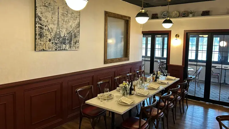 A dining room with dark wood paneling, a long table set for a party and pendant lights by tall windows