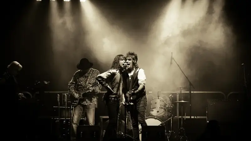 Sepia photo of the Classic Stones Live singer and guitarist sharing a microphone under bright stage spotlights