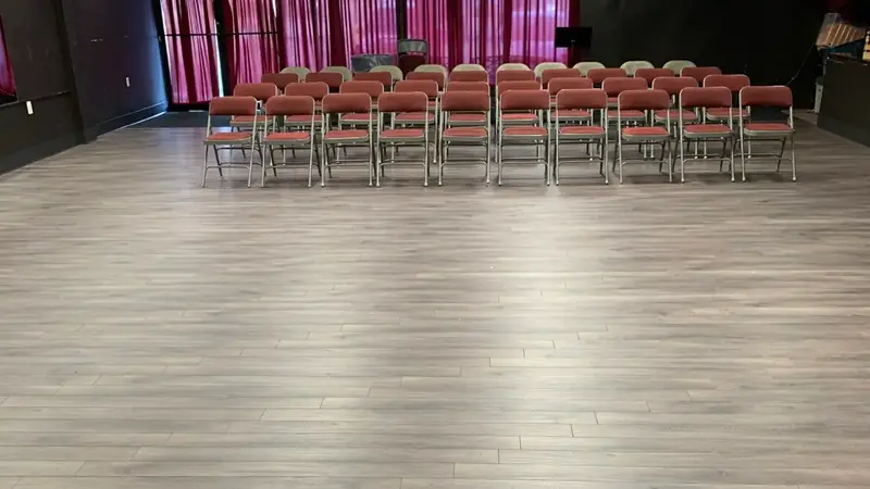 A smaller rental room with a light wood floor, red curtains and rows of red chairs