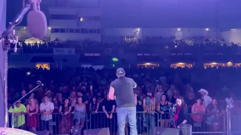 The Crash My Party singer on an outdoor stage, seen from behind, facing a large crowd at night