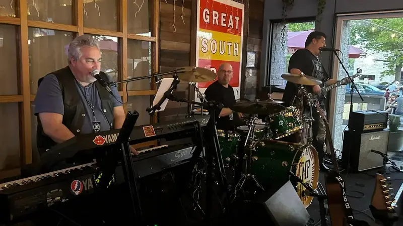 Crash My Party's keyboard player, drummer and guitarist playing inside a brewery with a Great South Bay sign