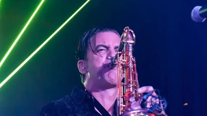 Decadia's saxophone player playing a gold tenor sax on stage under blue light and green lasers