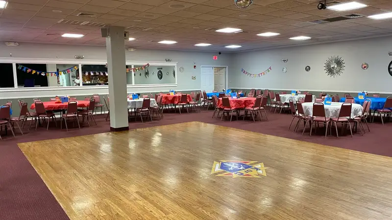 A banquet hall set up for a dance, with a wooden dance floor surrounded by tables with red and blue tablecloths