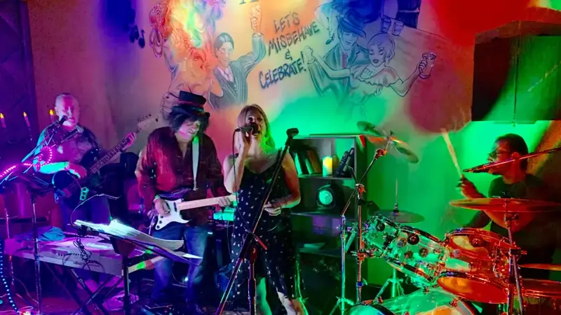 Electric Dudes playing on a small bar stage lit with bright purple, green and red lights