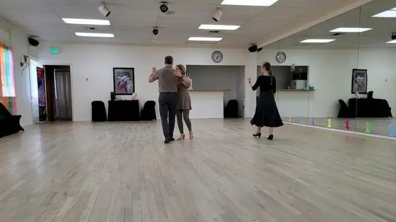 A couple dancing together during a lesson in the bright studio, with a woman in a black dress dancing nearby