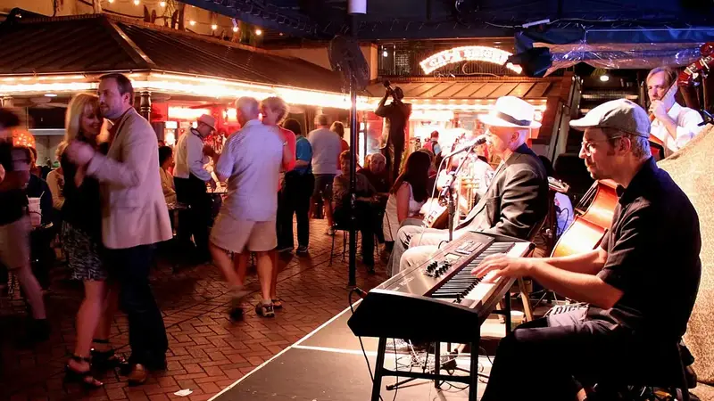 Couples dance on a brick patio at night next to a small stage where a band with a keyboard player performs