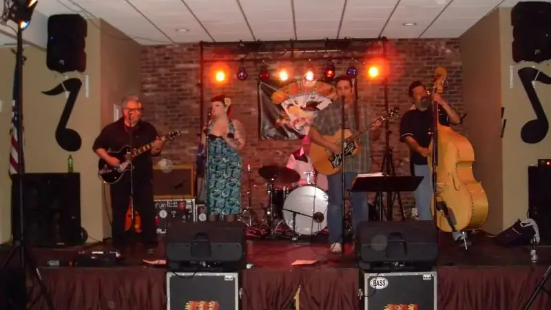 A rockabilly band with guitars, upright bass and a singer playing on the lodge's low stage in front of a brick wall under red stage lights