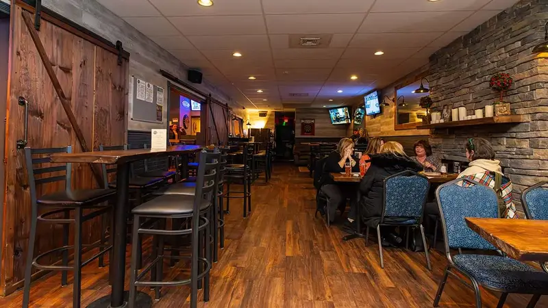 Inside Kitty Mulligan's: high-top tables on a wood floor, a stone wall with TVs and a barn door, with guests at tables