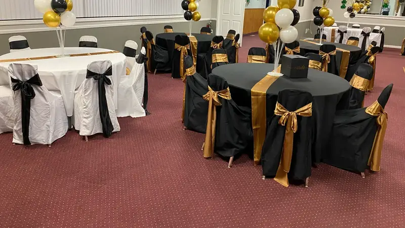 Round tables with black and white covers, gold sashes and black-and-gold balloon centerpieces in the hall