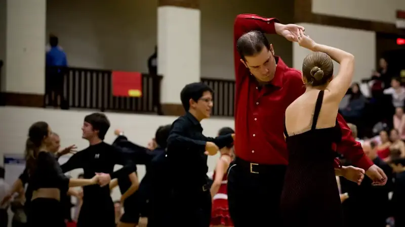 Couples in black and red dance at a college ballroom event in a gym; a man in a red shirt turns his partner under his arm