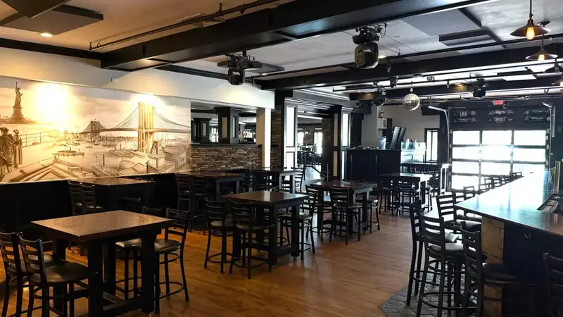The main bar room at Lily's with high-top tables on a wood floor, a Brooklyn Bridge mural, stage lights and a disco ball