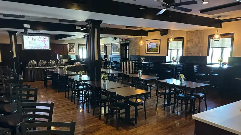 A dining room at Lily's with dark wood tables and chairs on a shiny wood floor and a buffet set up at the back