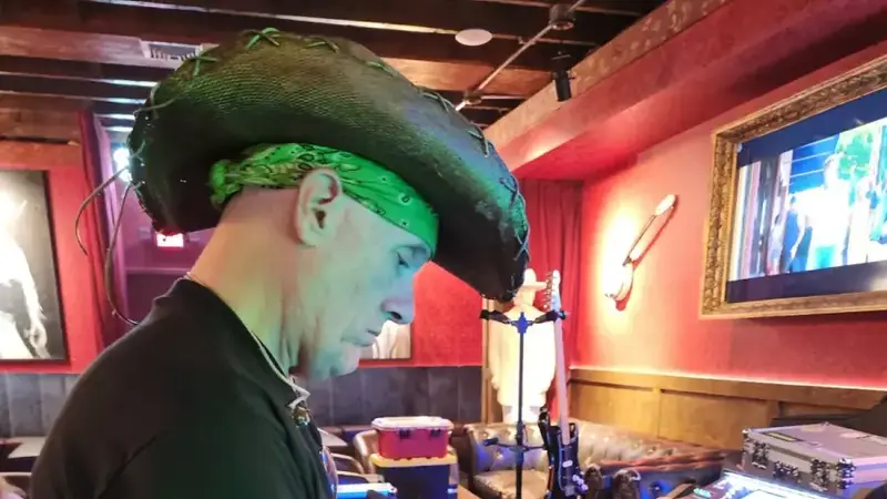 A Limewired keyboard player in a cowboy hat and green bandana playing keys at a bar gig