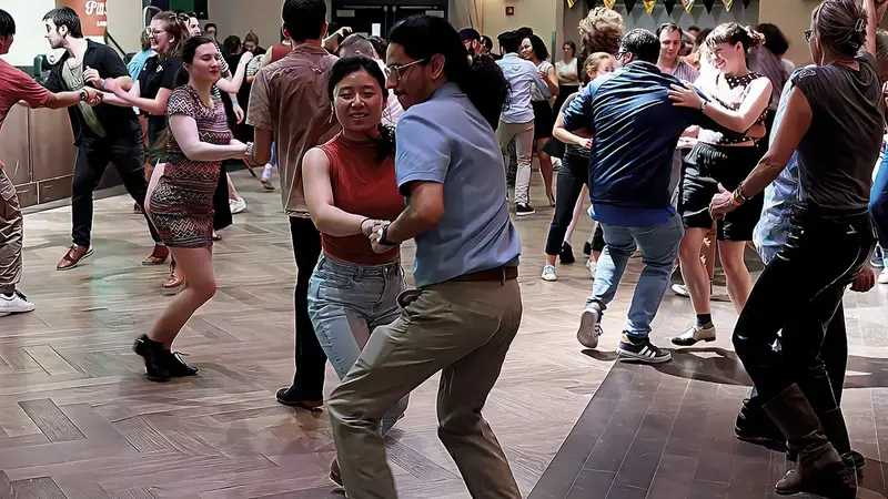 A smiling couple dances Lindy Hop in a close hold on a crowded social dance floor