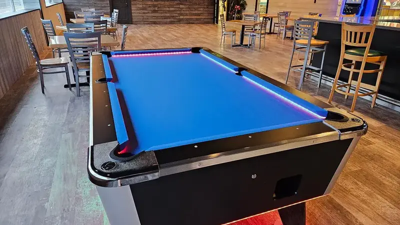 The lounge with a pool table, wood-panel walls, high-top tables and a bar along the side