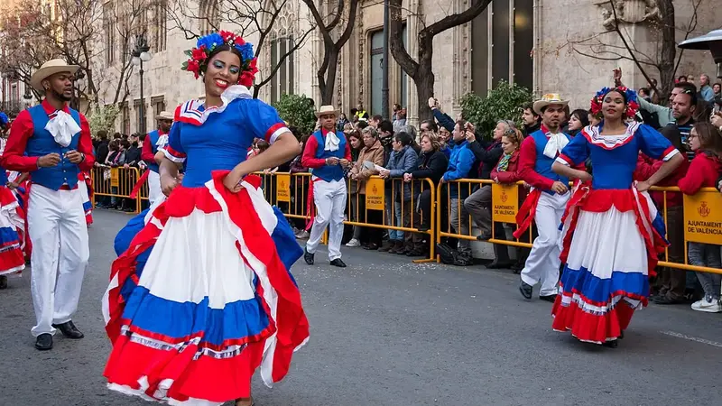 Dancers in red, white and blue Dominican folk costumes perform merengue in a street parade as a crowd watches
