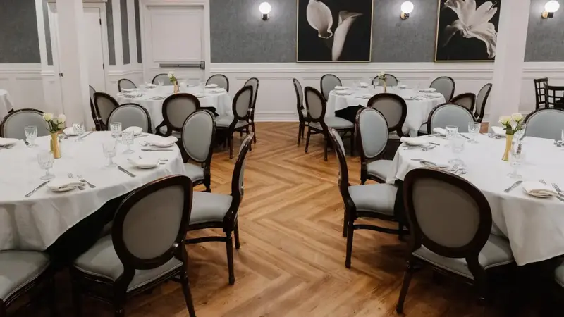 Mezza Luna's party room set with round tables, white tablecloths and gray chairs under globe lights