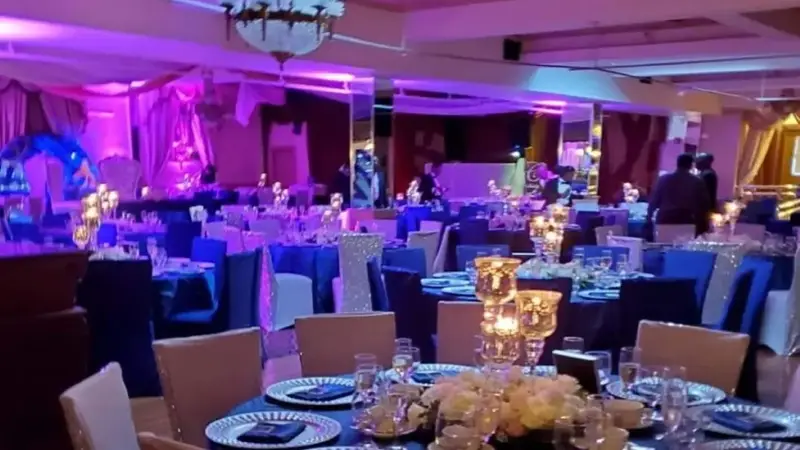 Mirelle's ballroom set for a party, with round tables, gold chair covers, candles and a chandelier under purple lighting