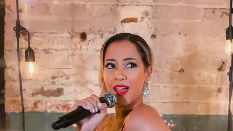Nitework's lead singer in a black sequined dress singing into a microphone in front of a brick wall