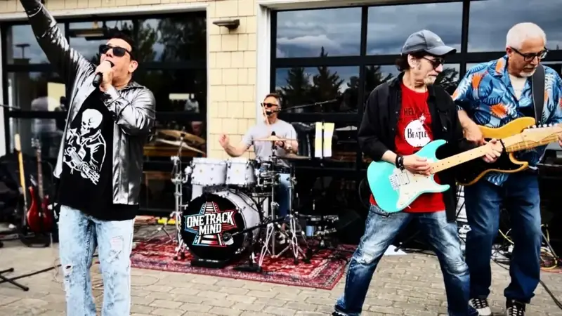 One Track Mind performing outdoors in front of a brewery, the singer raising his arm while two guitarists play