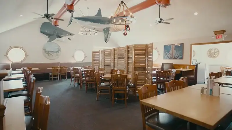 Popei's dining room with wooden tables and booths, ceiling fans and model sharks hanging from the ceiling