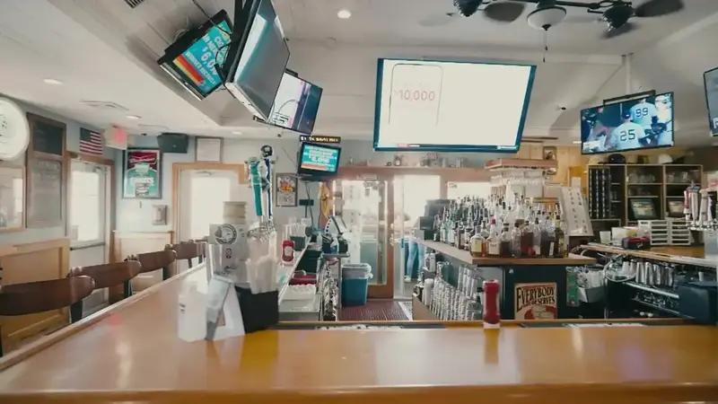 The long bar at Popei's with a wooden counter, TV screens above and shelves of bottles