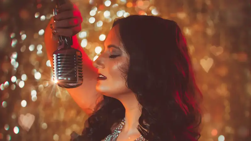 Promo photo of Renee D'Angelo holding a vintage microphone in front of sparkling gold lights
