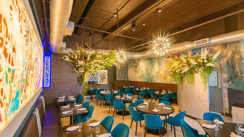 Revel's dining room with teal chairs, a large colorful mural, flower arrangements and sparkly hanging lights