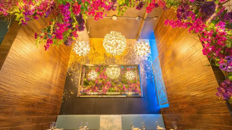 A private dining nook at Revel framed by pink flowers, with round crystal chandeliers and a long table