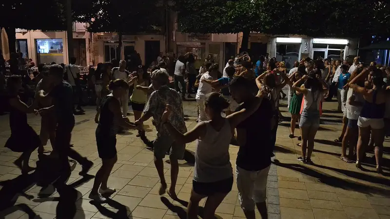Couples dance salsa at night on a town square under the trees during a summer music festival