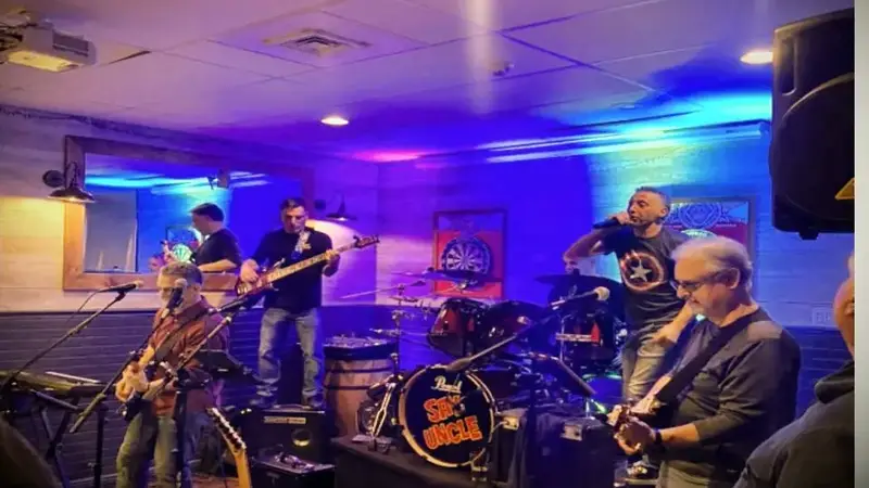 Say Uncle performing in a pub under blue and purple lights, with the band name on the bass drum