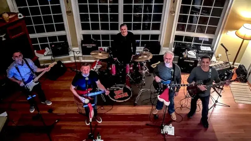 Overhead view of the six members of Say Uncle with guitars, drums and keyboards set up in a big room with tall windows