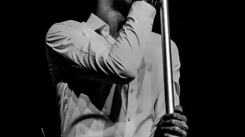 Black-and-white photo of the Strangelove singer in a white shirt gripping a microphone stand