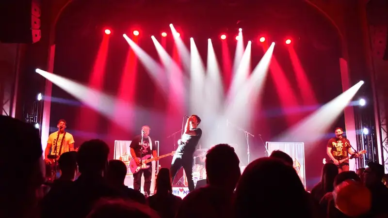 A rock band plays on the Suffolk Theater stage under red and white spotlights, seen from behind the crowd
