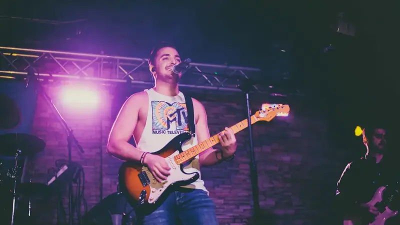 The 90's Band's guitarist singing and playing on a stage lit with purple lights