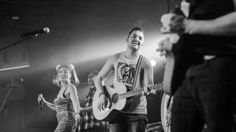 Black-and-white photo of The 90's Band performing, with the singer and an acoustic guitarist at the front of the stage
