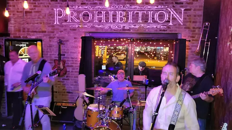 The Byrne Unit singing and playing guitar in front of a brick wall with a pink neon Prohibition sign in Massapequa