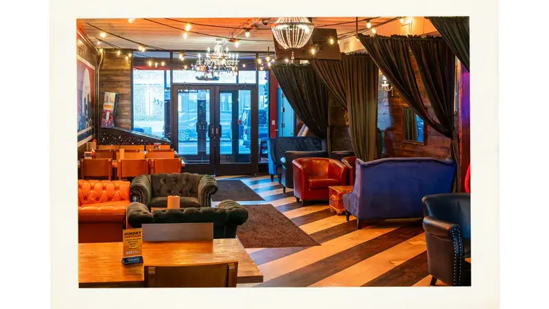 The lounge with leather sofas and armchairs, dark curtains and string lights near the front windows