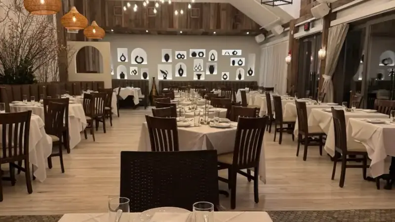 The Cove's main dining room with white-clothed tables, hanging pendant lights and a high wood ceiling