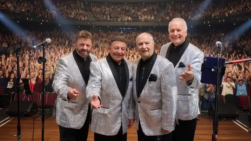 The Fabulous Acchords in silver jackets on a theater stage in front of a large audience
