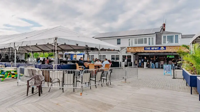 The open dock area at The Spot with a white tent, tables and chairs, and the tiki bar beside the marina building