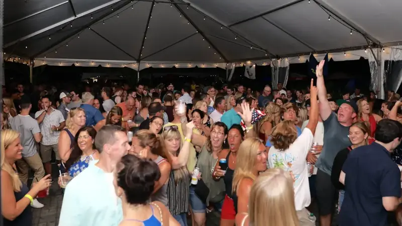 A big crowd dancing and cheering under the string-lit tent at The Spot during a night band show
