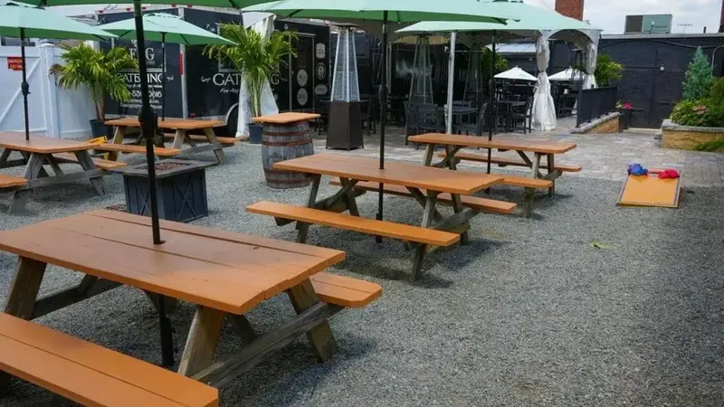 Wooden picnic tables on gravel under green umbrellas in The Villager's outdoor beer garden