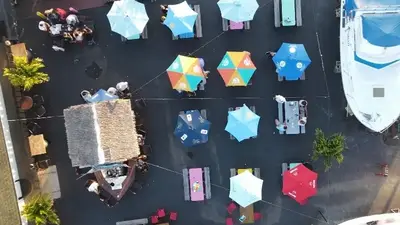 Aerial view of Toomey's outdoor patio with colorful umbrellas, picnic tables, a thatched tiki bar and boats docked alongside