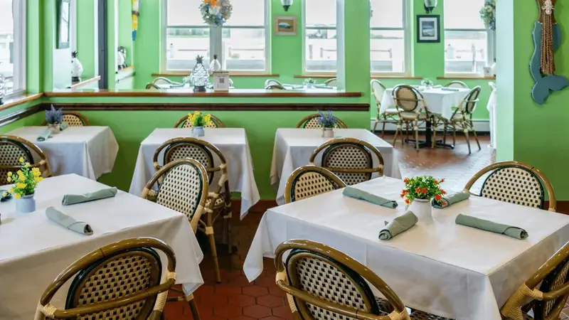 Inside Tres Palms: a bright green dining room with white tablecloths, wicker-back chairs and windows on the water