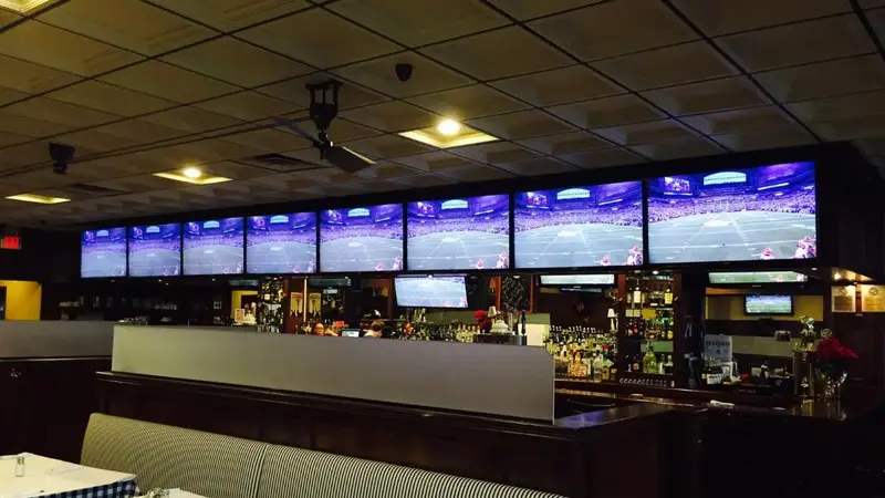 Inside Trotters: a long bar under a row of big TV screens, with booths and checkered tablecloths in front